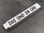 White folding ruler laid diagonally on a dark textured surface, showing the 20 cm marking