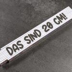 White folding ruler laid diagonally on a dark textured surface, showing the 20 cm marking
