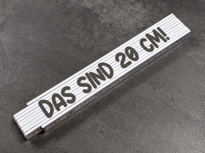 White folding ruler laid diagonally on a dark textured surface, showing the 20 cm marking