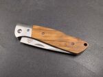 Partially opened folding knife with a wooden handle resting on a dark textured surface, showing a metal blade and screws along the handle.